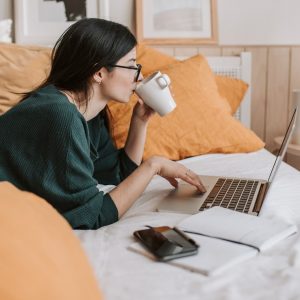 female-with-glasses-drinking-coffee-while-browsing-laptop