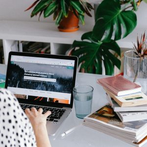 person-browsing-laptop-with-water-glass-and-book-stack