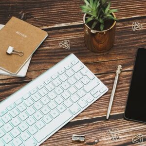 Mac-kayboard-gold-pen-side-of-ipad-brown-gold-notepad-gold-plant-pot-green-spikey-leaves-on-a-brown-wooden-desk