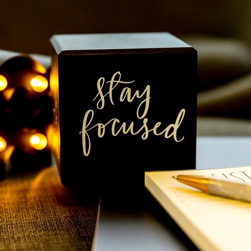 stay-focused-black-cube-with-notepaper-pen-glass-lights-grey-chair-in-bg