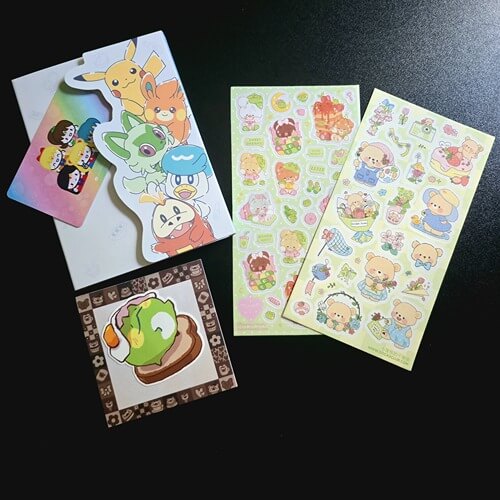 sailor moon washi card on pokemon memo pad, frog sitting on bread with egg on head on top of brown bordered mini memo, bear stickers on black background